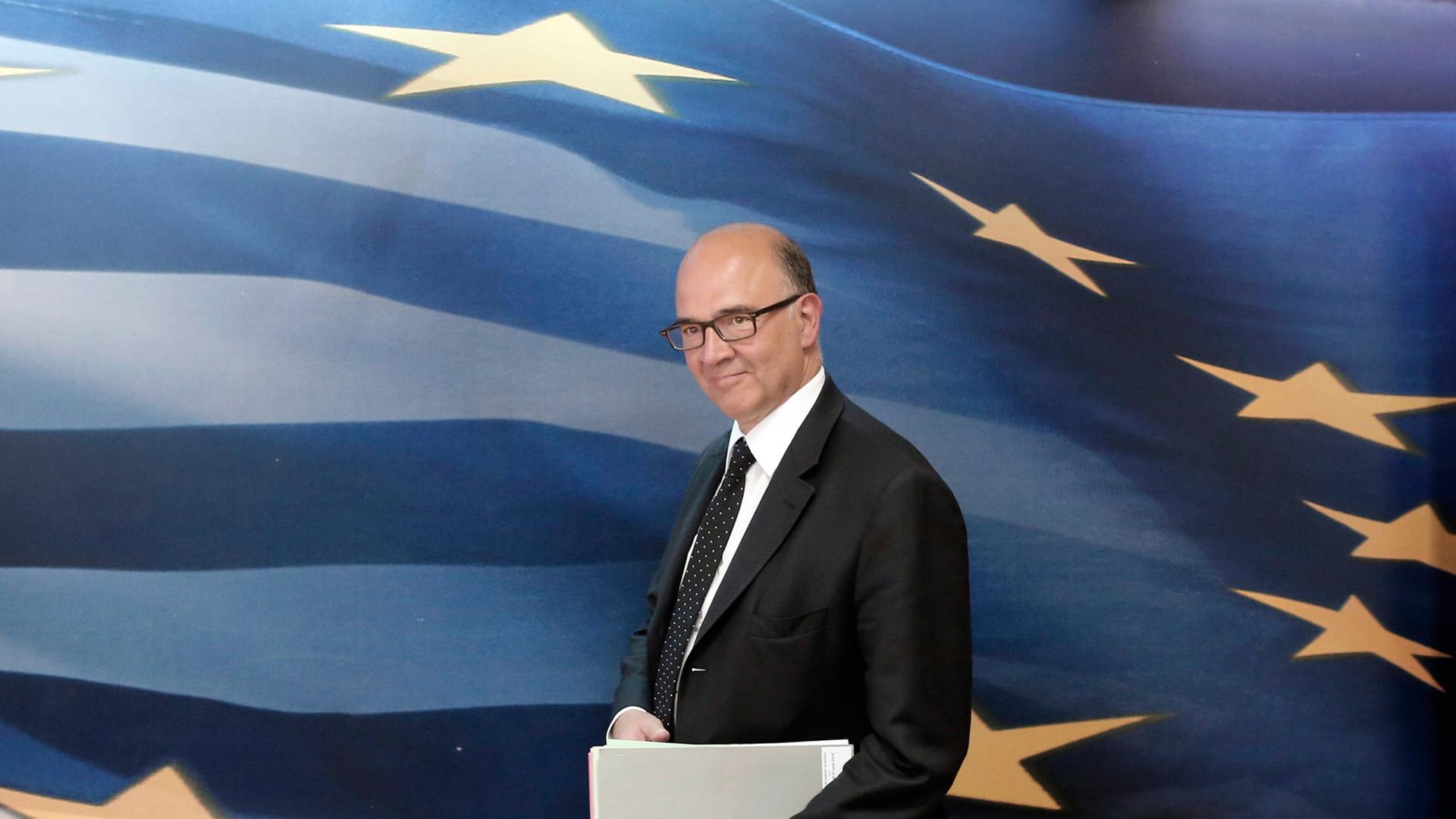 Frankreichs ehemaliger Finanzminister und Kandidat für die EU-Kommission Pierre Moscovici, geht vor einer großen blauen EU-Flagge mit gelben Sternen und weißen Streifen entlang