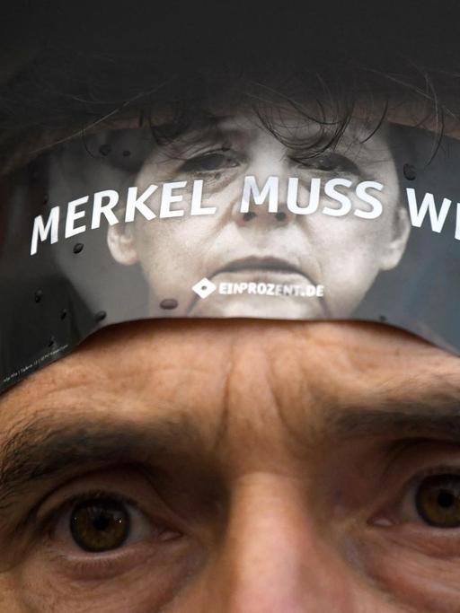 Ein Demonstrant protestiert am 06.09.2017 in Finsterwalde (Brandenburg) auf dem Marktplatz gegen Bundeskanzlerin Angela Merkel (CDU) während einer Wahlkampfveranstaltung der CDU mit einem Aufkleber auf seiner Stirn. Foto: Ralf Hirschberger/dpa-Zentralbild/ZB | Verwendung weltweit