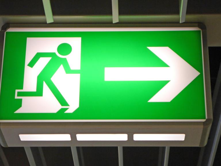 Eine grünes Notausgangs-Hinweisschild mit einem grünen Männchen und einem weißen Pfeil, der nach rechts zeigt.