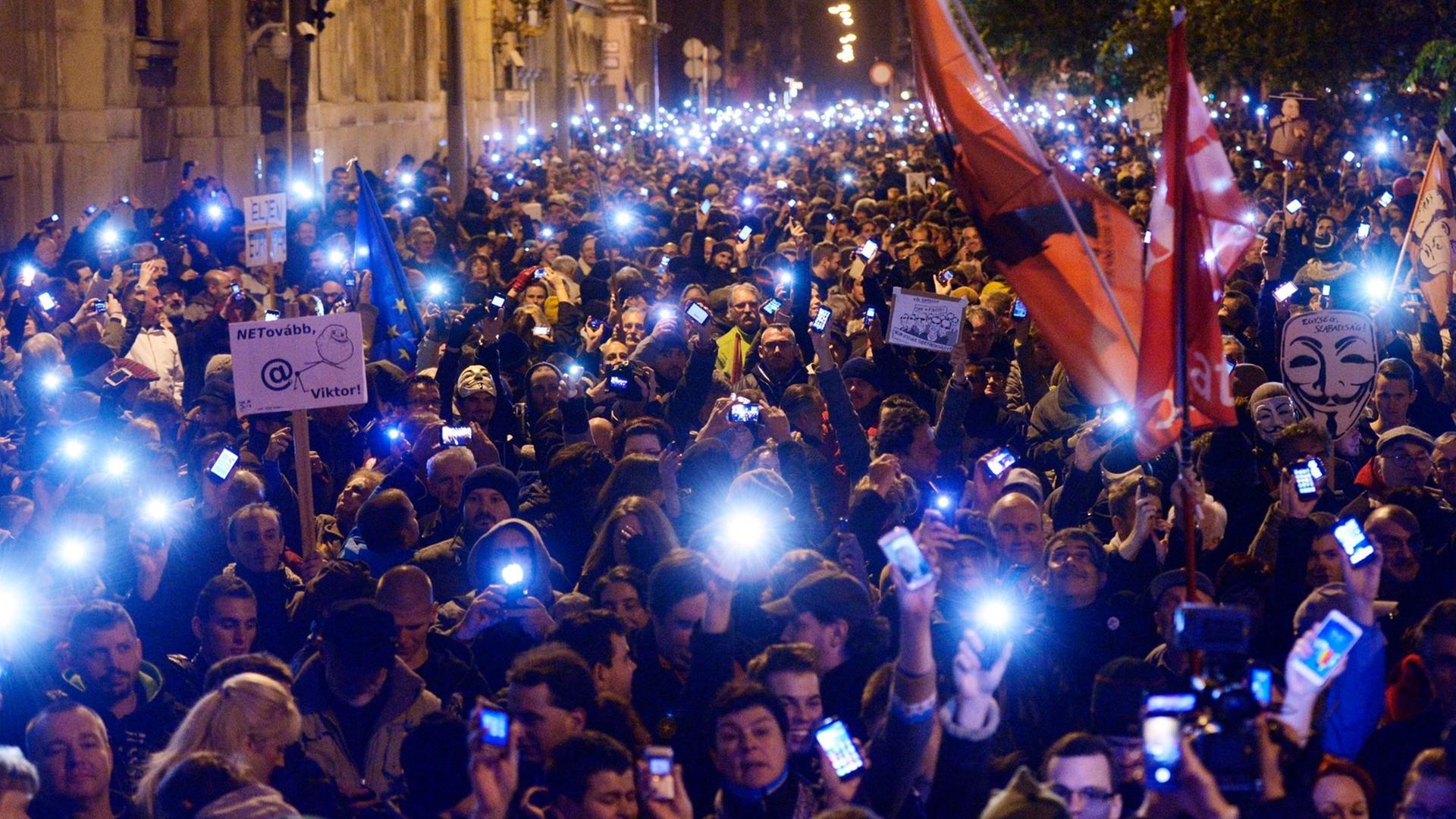 Demonstranten laufen im Dunkeln mit Lichtern in den Händen über eine Brücke in Budapest.