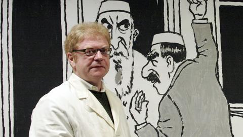 Der Karikaturist Achim Greser vor einer Plakatwand im Frankfurter U-Bahnhof am Willy-Brandt-Platz, die einen Mann mit "orientalisch-mediterraner Leidenschaft" zeigt, der in der U-Bahn seinem Gegenüber "Dschihad" (Heiliger Krieg) zuruft - die Antwort lautet "Gesundheit".