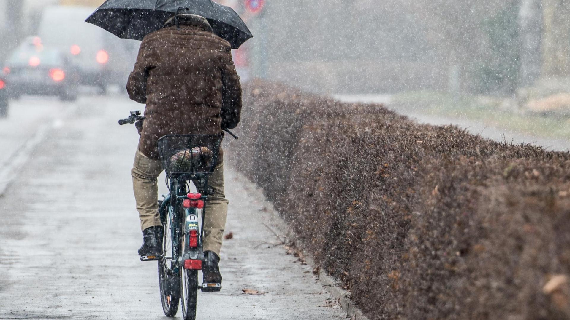 Ein Mann mit Regenschirm fährt Fahrrad im Schneeregen