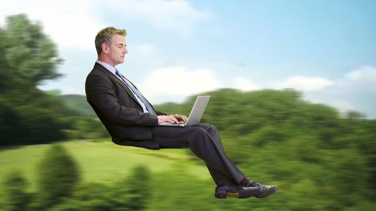 Ein Geschäftsmann schaut sitzend auf seinem Laptop, der Zug in dem er sitzt ist herausretuschiert, er ist nur von Landschaft umgeben (Bild: Bewegtes Land)