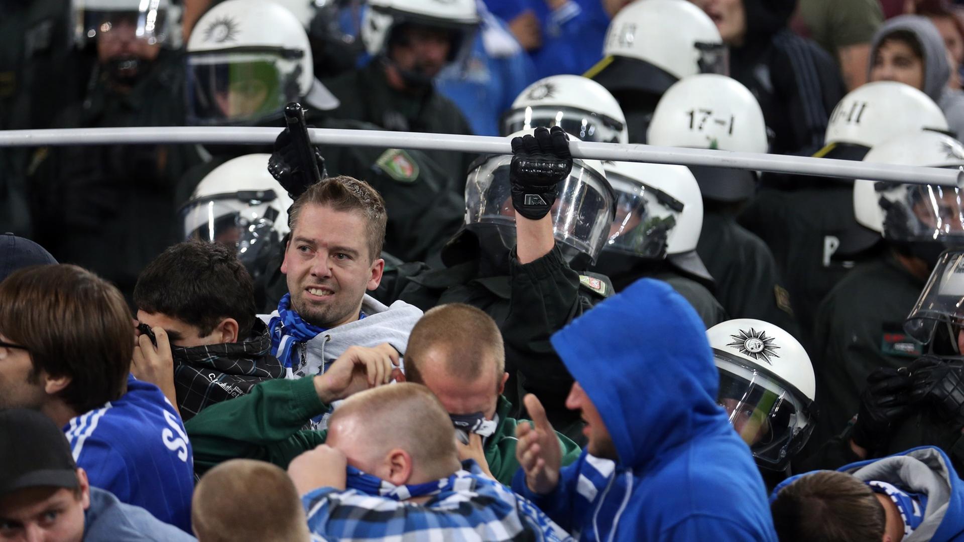 Auf dem Bild sieht man Polizisten mit Schutzhelmen in einer Menge von Fußball-Fans