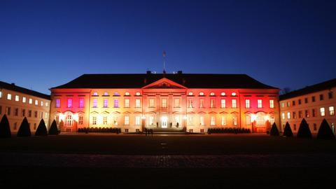 Das Schloss Bellevue wird im Dunkeln gelb und rot angestrahlt.  