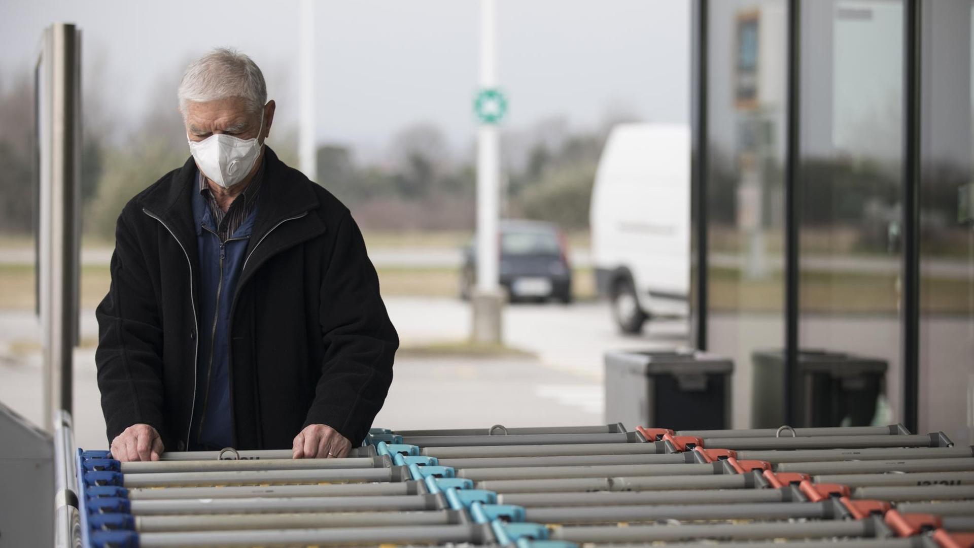 Ein älterer Mann mit Atemschutzmaske nimmt sich einen Einkaufswagen.