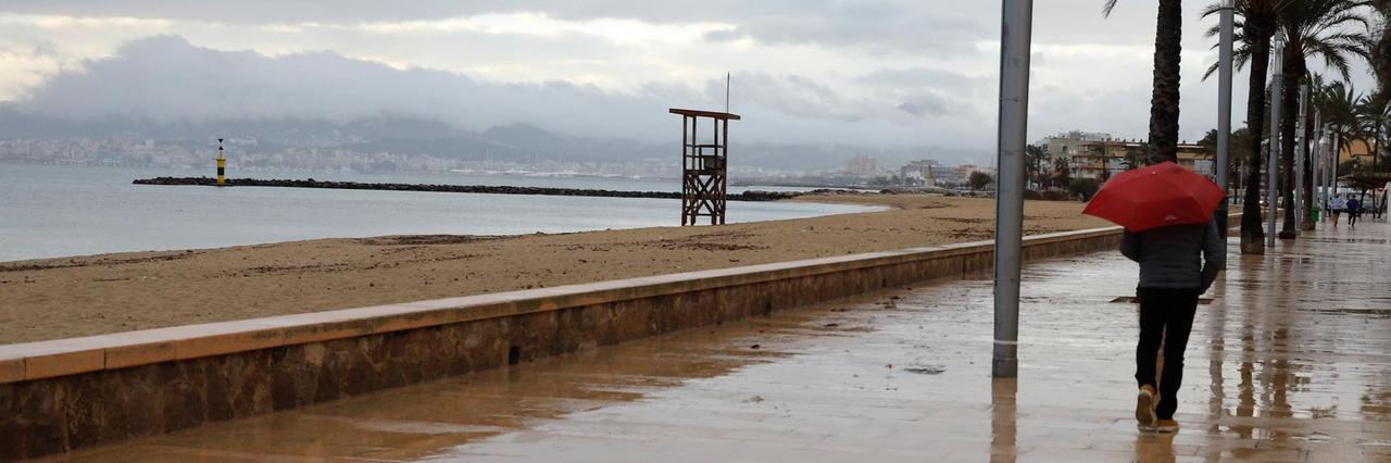 Ein Mann spaziert mit einem Regenschirm am Strand von Palma entlang. 