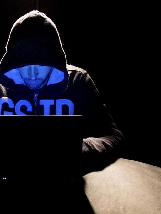 Ein Hacker mit Kapuzenpulli sitzt vor seinem Laptop.