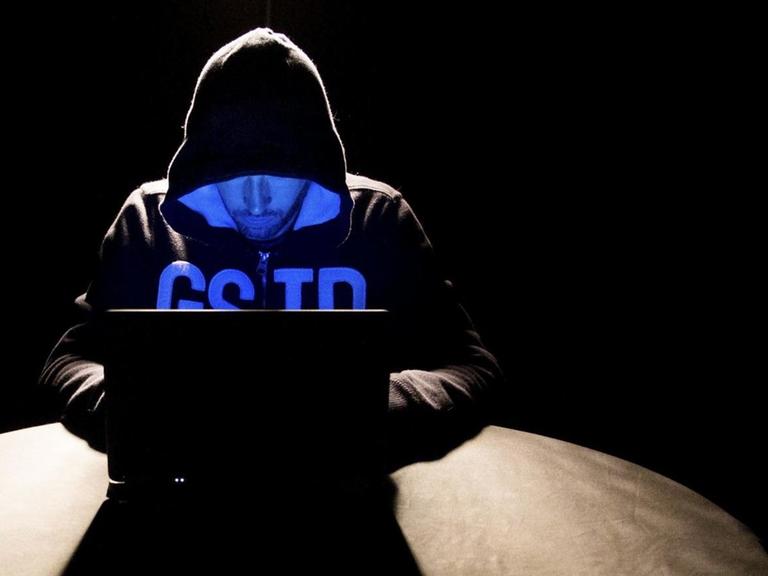Ein Hacker mit Kapuzenpulli sitzt vor seinem Laptop.