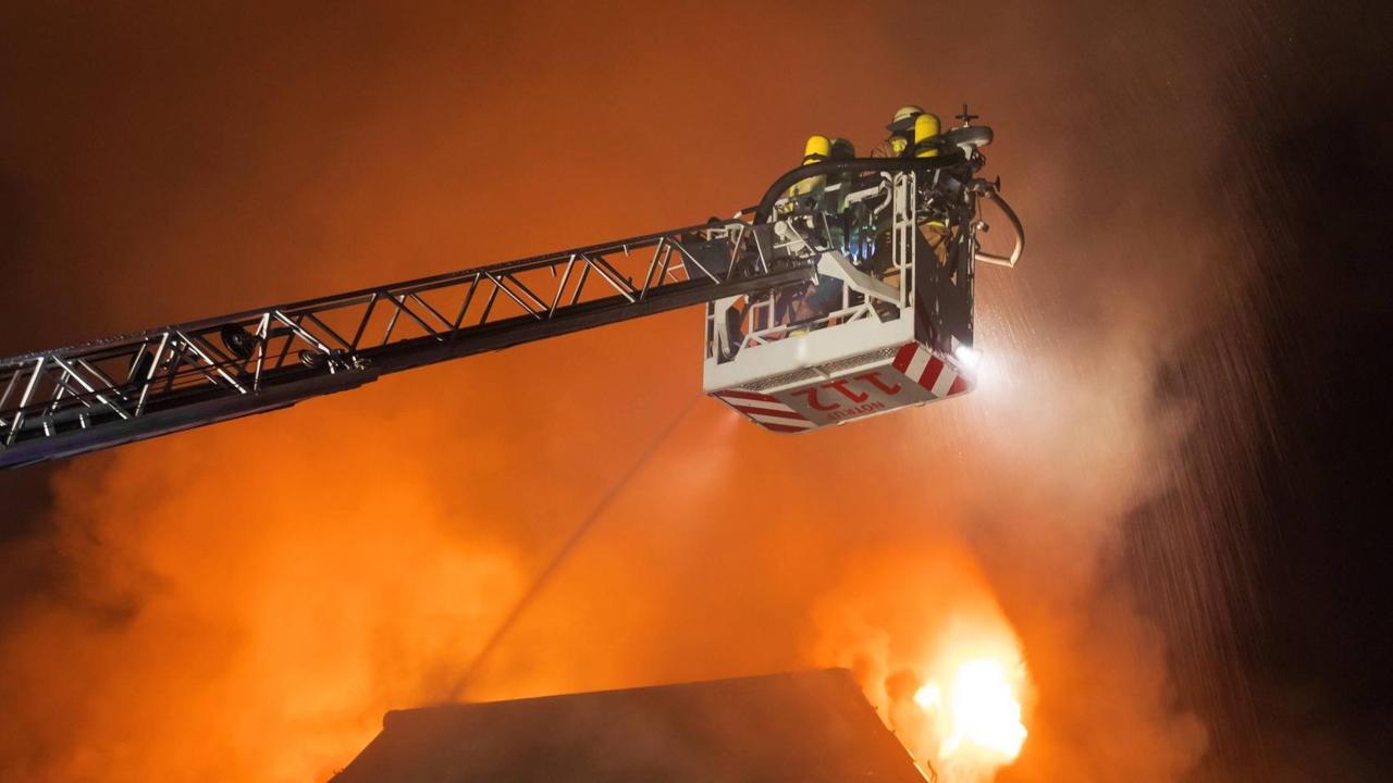 Feuerwehrleute der Feuerwehr Berlin bei einem Löschangriff in einer Drehleiter über einem brennenden Dachstuhl in Berliner Bezirk Wilmersdorf in der Nacht zum 25.07.2018.