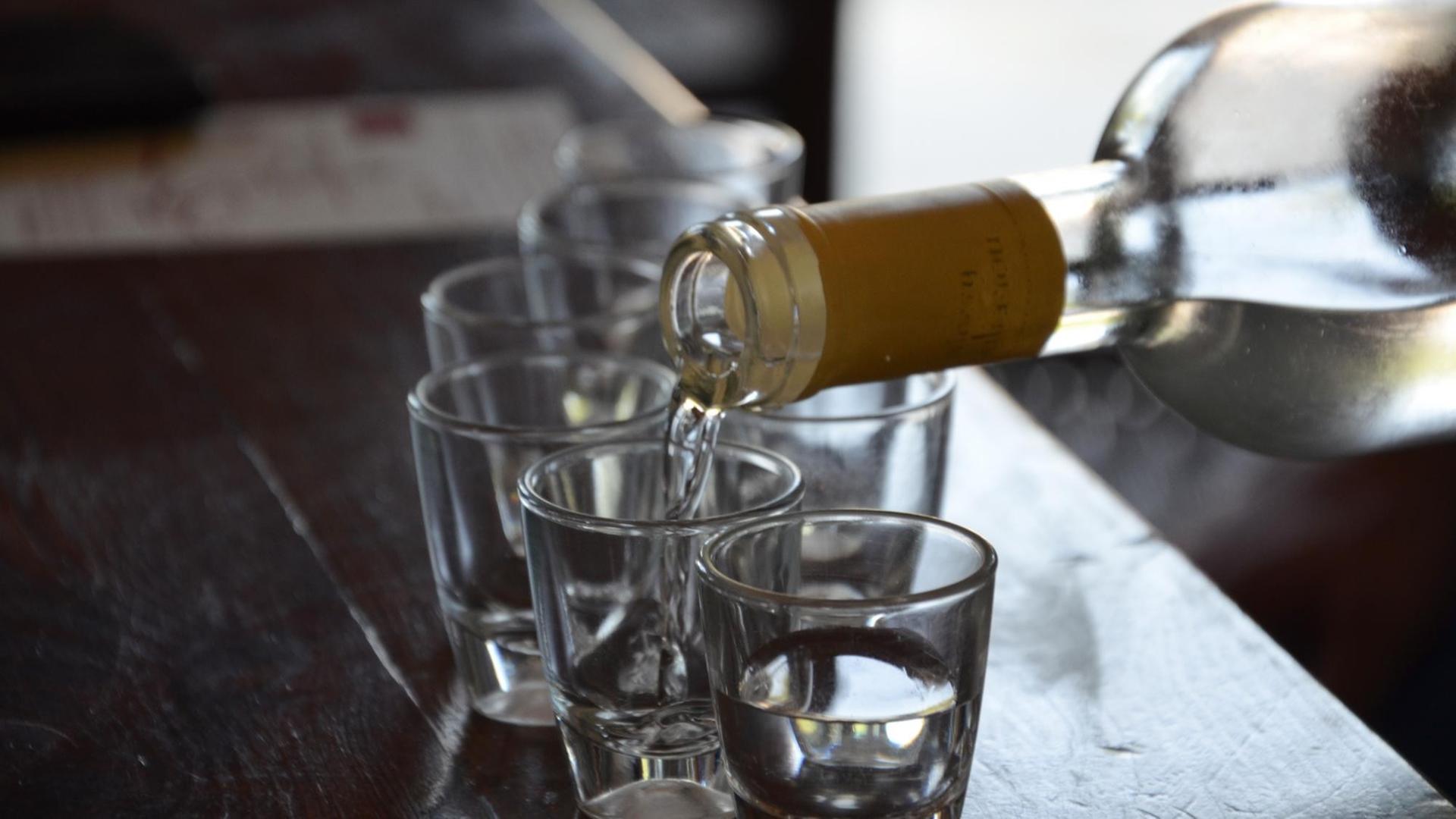 Alkohol wird aus einer Flasche in kleine Schnapsgläser gefüllt. Alkohol wird aus einer Flasche in kleine Schnapsgläser gefüllt.