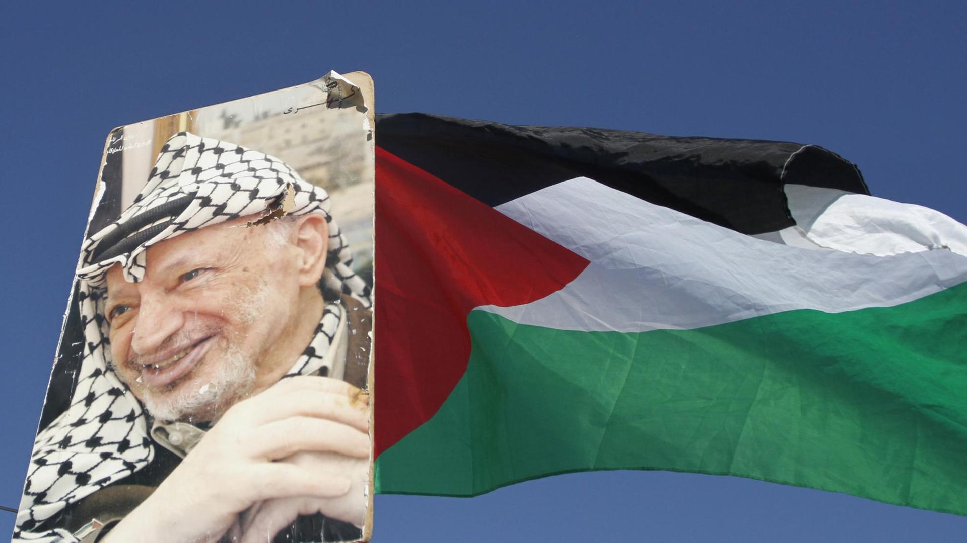 Ein Porträt von Palästinenserpräsident Arafat neben einer palästinensischen Flagge.