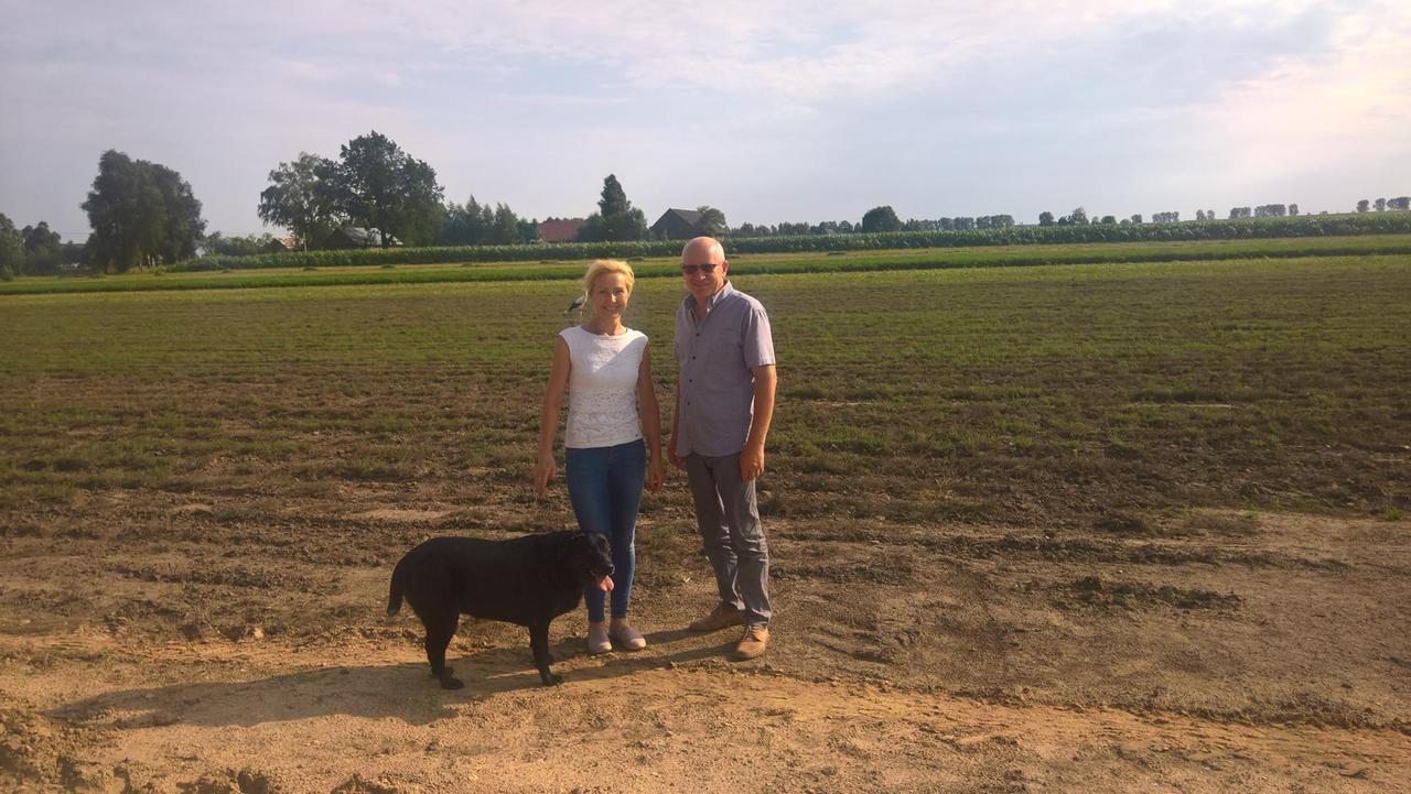 Das Ehepar Romaniuk steht auf einem Feld mit Hund und lacht.