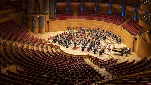 Ein Orchester, von schräg oben betrachtet, spielt vor leeren Zuschauerrängen.