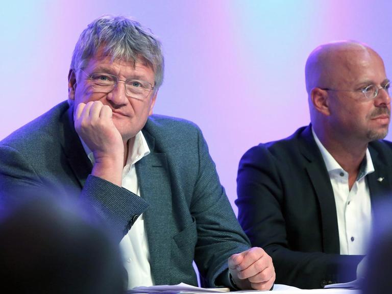 Jörg Meuthen und Andreas Kalbitz sitzen sitzen hinter einem Pult und blicken in unterschiedliche Richtungen.