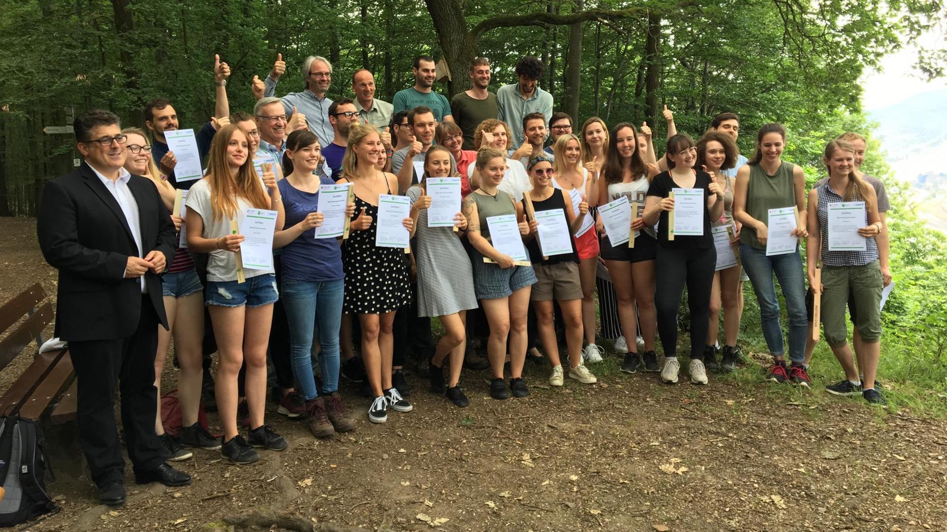 40 Umwelt- und Klimaschutz-Studenten stehen in einem Wald und halten ihre Urkunden in ihren Händen