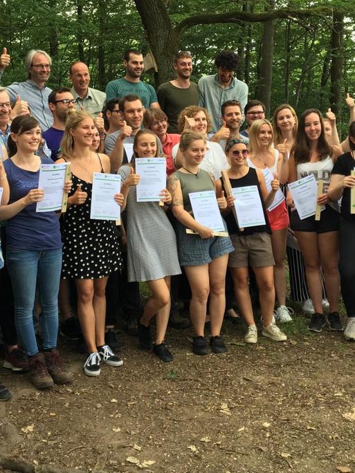 40 Umwelt- und Klimaschutz-Studenten stehen in einem Wald und halten ihre Urkunden in ihren Händen