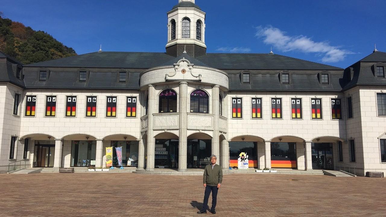 Herr Mori leitet das Deutsche Haus in Naruto. Er steht vor diesem weißen Gebäude mit deutschen Flaggen in den Fenstern.