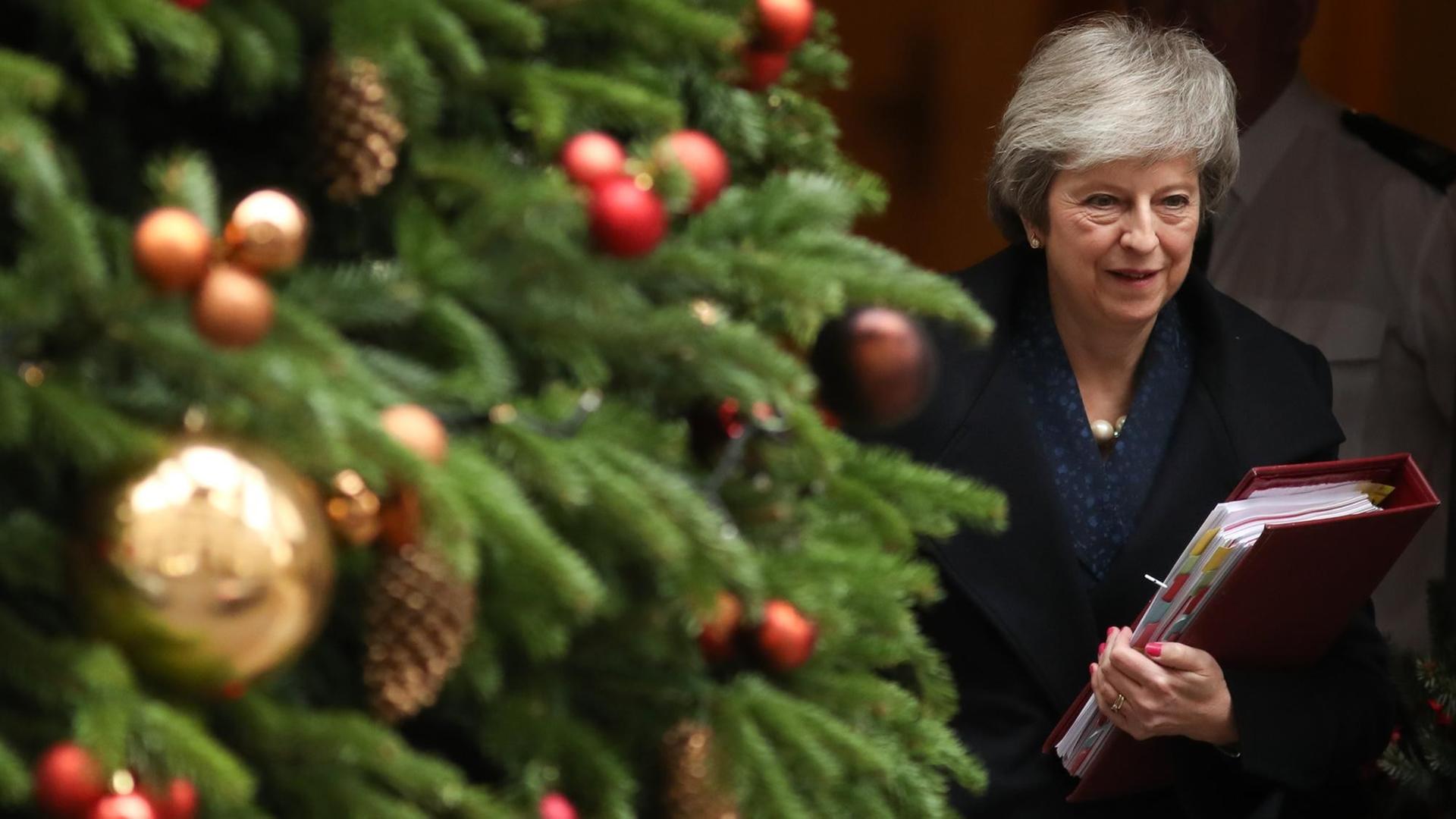 Theresa May geht mit Dokumentenmappe in der Hand an einem geschmückten Weihnachtsbaum vorbei.