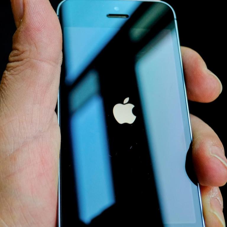 Eine Hand hält ein schwarzes iPhone. Auf dem Display ist das Apple-Logo, ein weißer Apfel, zu sehen.