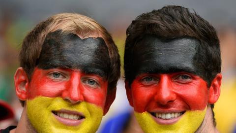 Zwei junge Männer mit in den Deutschlandfarben schwarz, rot und gold geschminkten Gesichtern und Deutschland-Fußballtrikots