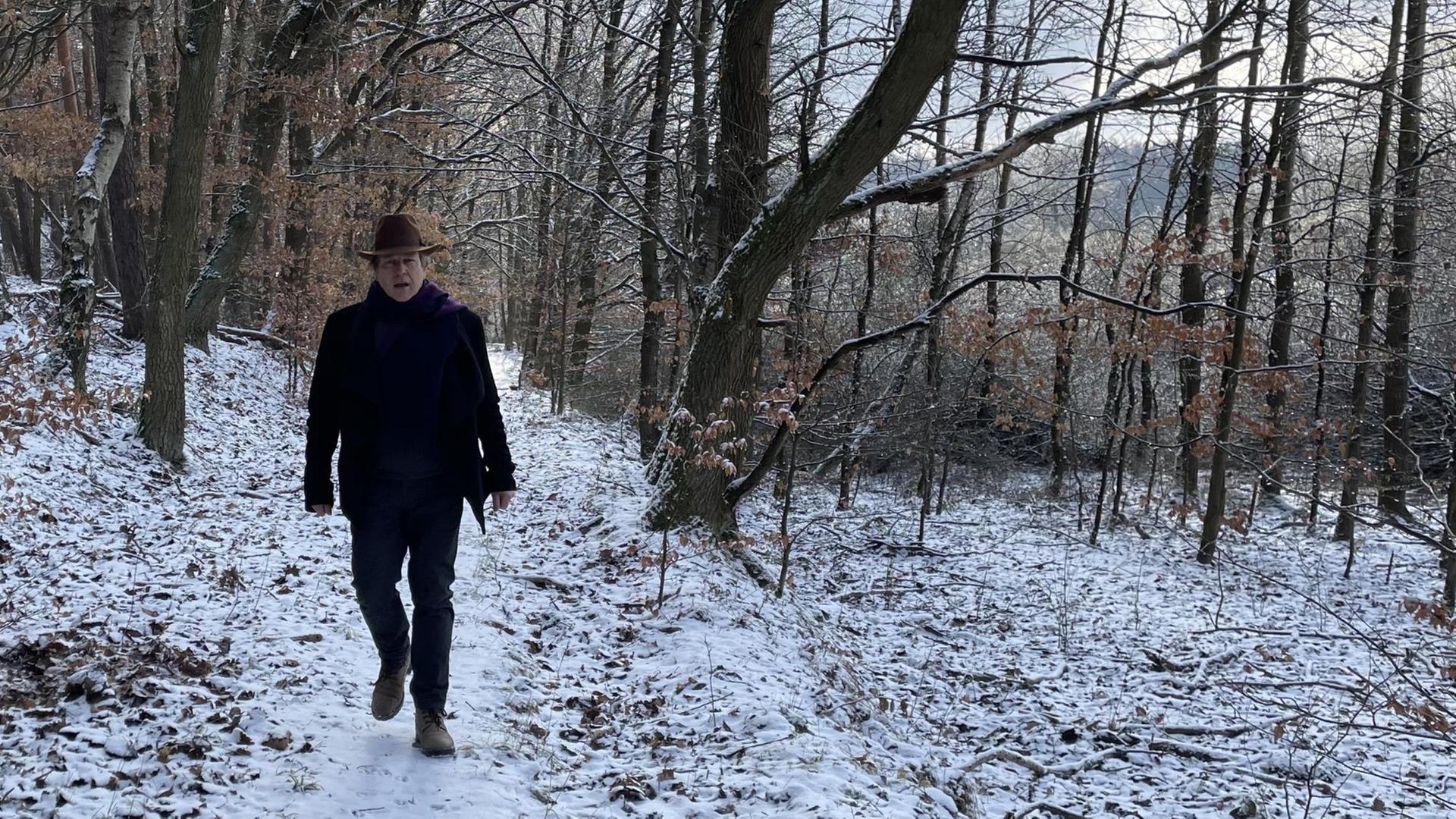 Ein Mann mit Hut läuft durch einen schneebedeckten, lichten Wald.