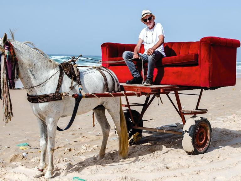 Horst Wackerbart mit seiner Couch auf einer Pferdekutsche an einem Strand im Senegal 2020.