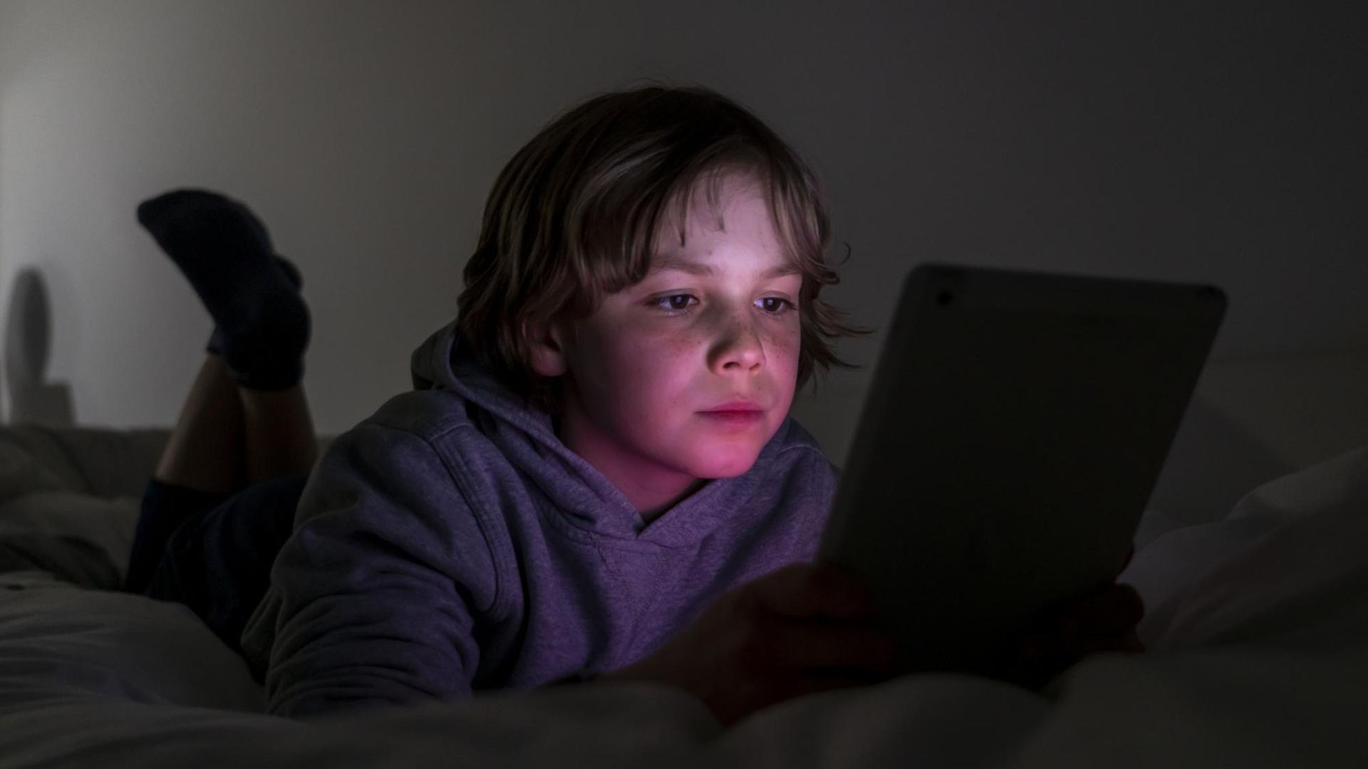 Ein Junge liegt auf einem Bett und spielt Computerspiele an einem Tablet.