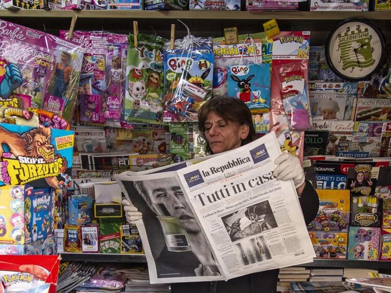 Eine Zeitungsverkäuferin in einem Kiosk in Italien hält einen Zeitungstitel hoch:"Tutti a casa" ("Jeder zu Hause") in Salerno, Italien am 10.März 2020