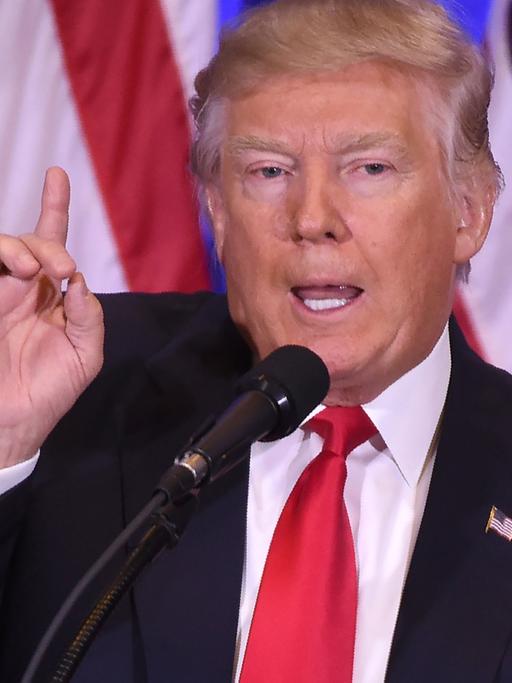 Donald Trump steht bei seiner ersten Pressekonferenz am 11.01.2017 im New Yorker Trump Tower mit erhobenem Zeigefinger vor mehreren US-Flaggen.