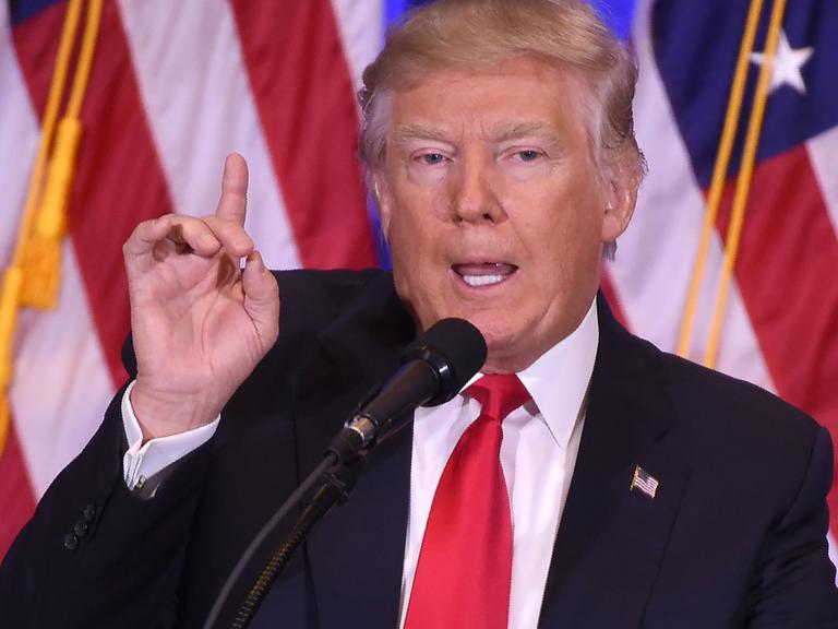 Donald Trump steht bei seiner ersten Pressekonferenz am 11.01.2017 im New Yorker Trump Tower mit erhobenem Zeigefinger vor mehreren US-Flaggen.
