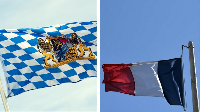Zwei Fahnen wehen im Wind. Links die Flagge des Freistaats Bayern, rechts die Flagge Frankreichs. Montage von zwei Fotos.