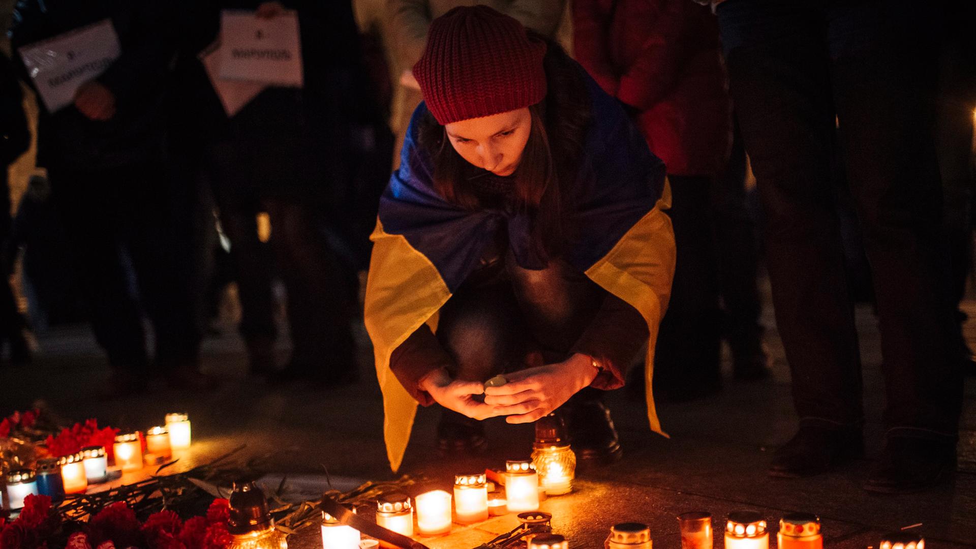Ein Mädchen trägt eine ukrainischen Flagge über den Schultern und stellt eine Kerze für die Opfer des Raketenangriffs in Mariupol auf der Straße ab.