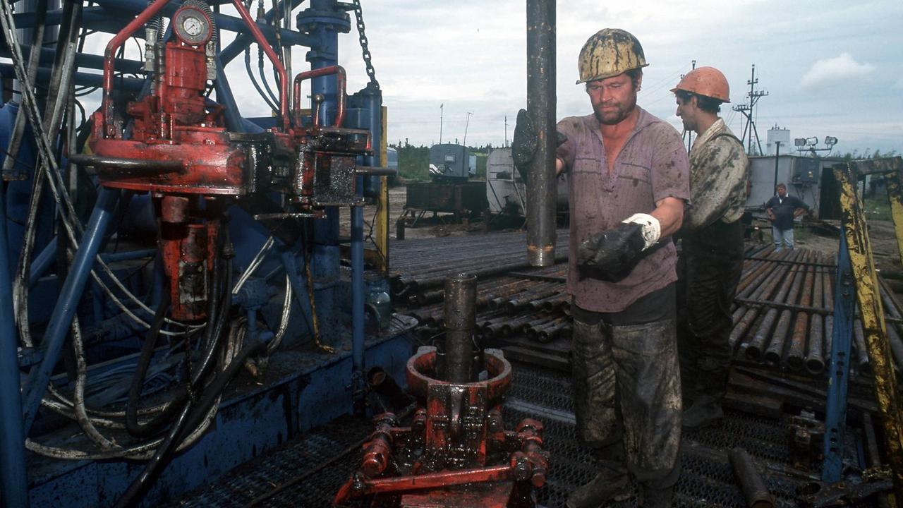 Mineralölförderung auf einem Ölfeld in Nefteyugansk in West Sibirien. Zwei Männer mit Helm arbeiten im Öldreck.
