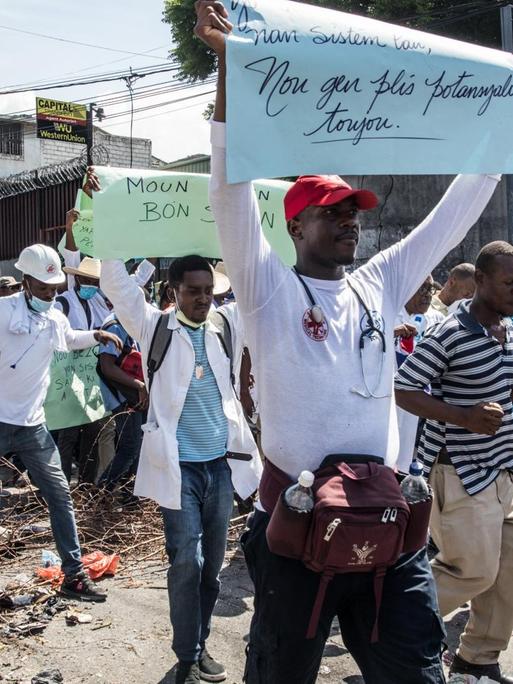 Menschen laufen in Port-au-Prince, der Hauptstadt von Haiti, in einer Demonstration mit. Auf ihren Schildern fordern sie den Rücktritt von Präsident Jovenel Moise.