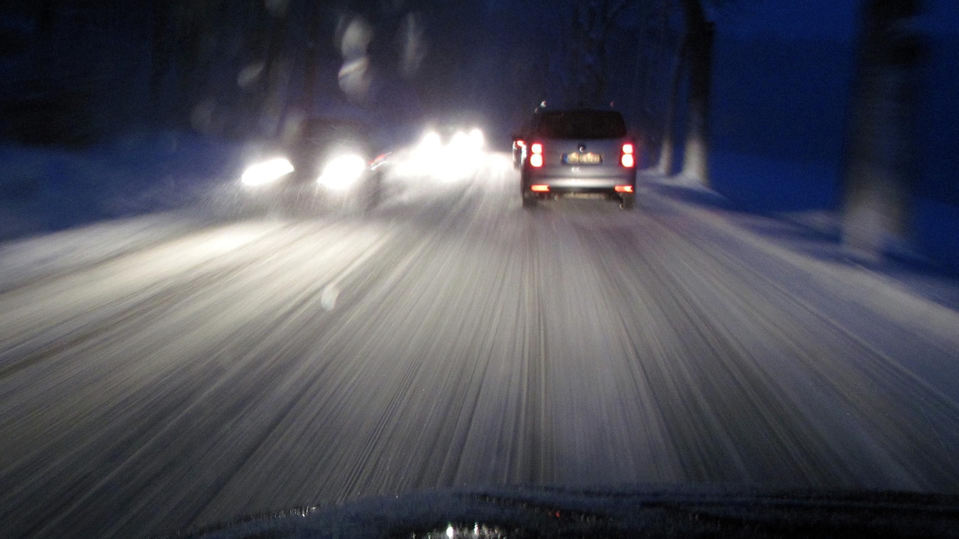 Blick durch eine Autoscheibe auf eine schneeglatte Straße im Dunkeln.