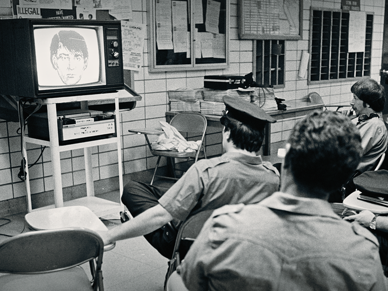 Polizisten sitzen vor einem Röhrenfernseher und schauen Phantombild an.