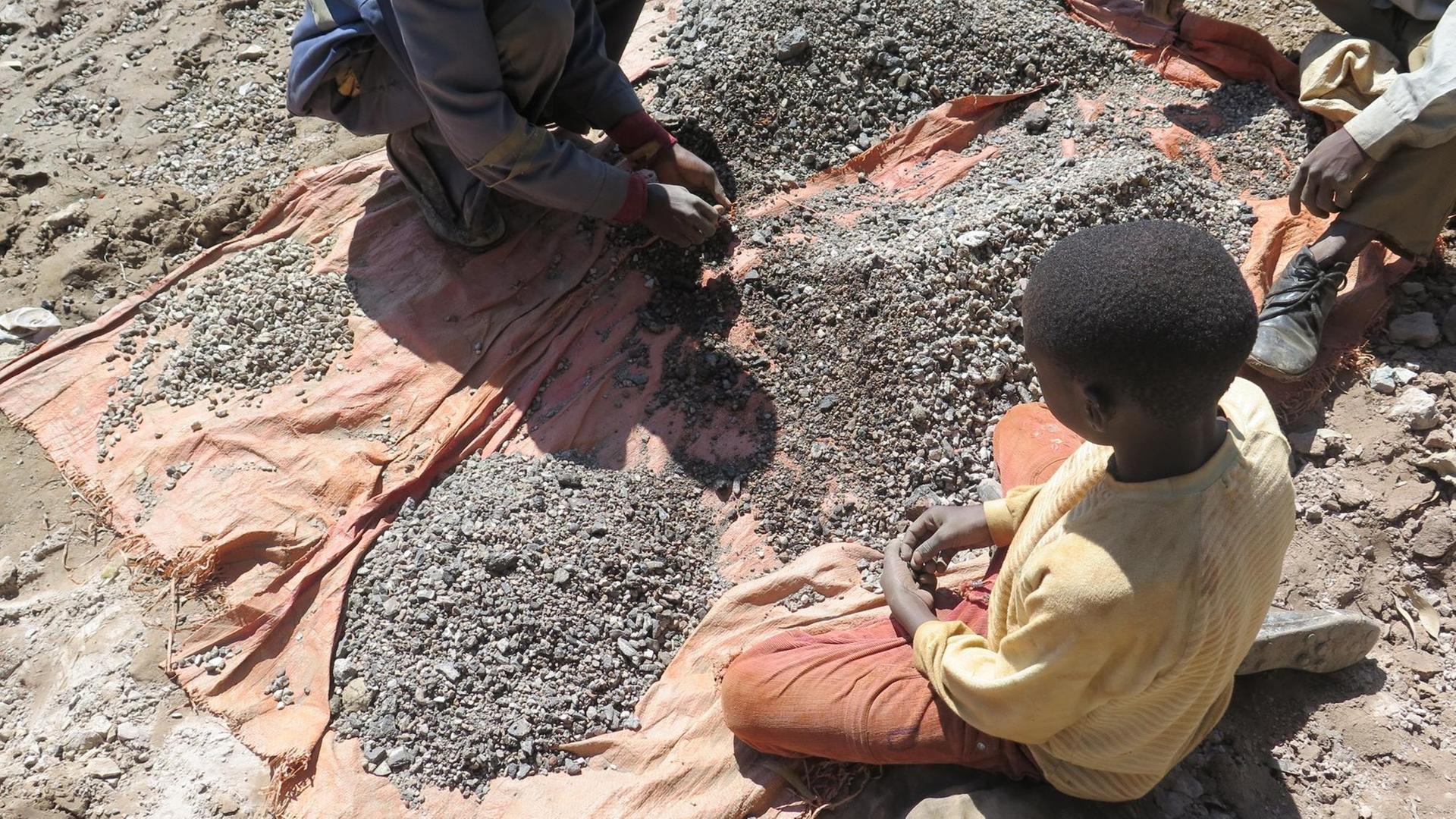 Kinder arbeiten auf dem Boden sitzend in einer Kobaltmine im Kongo.