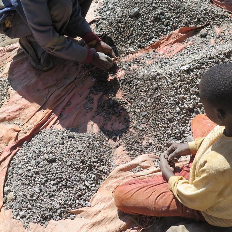 Kinder arbeiten auf dem Boden sitzend in einer Kobaltmine im Kongo.