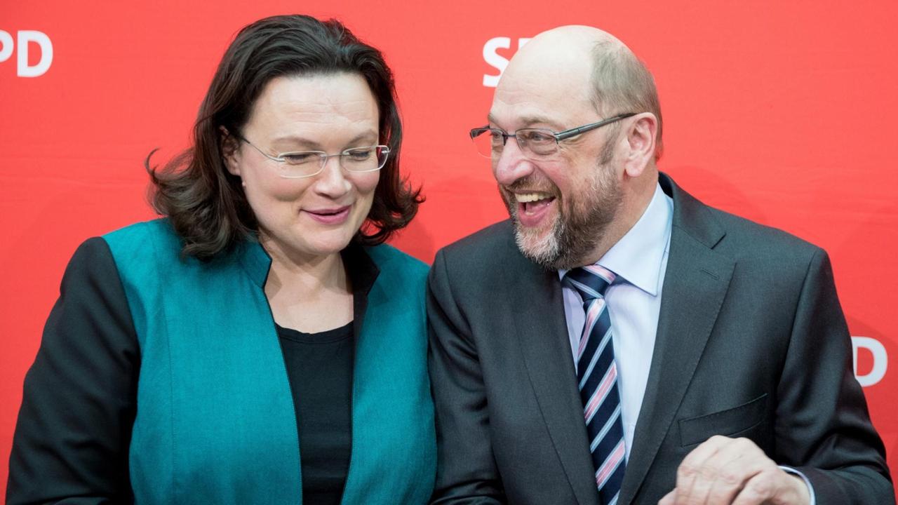 Nahles und Schulz stehen vor einer roten Wand mit dem SPD-Logo und lachen sich zu. 