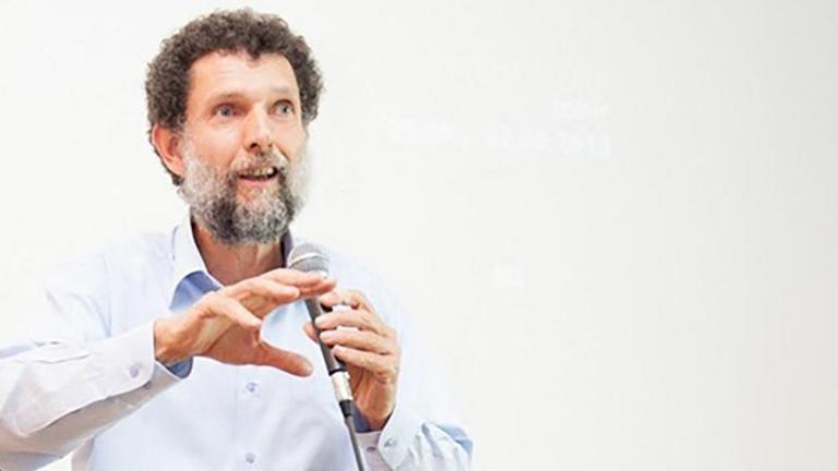 Das Bild zeigt Osman Kavala während eines Vortrags mit einem Mikrofon in seiner linken Hand.