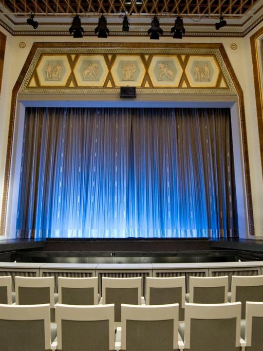 Blick in einen leeren Theatersaal mit geschlossenem Vorhang.