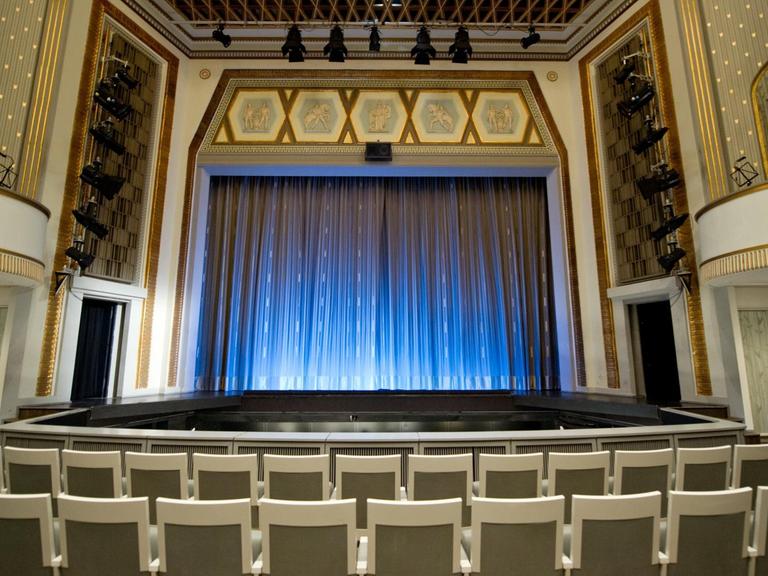 Blick in einen leeren Theatersaal mit geschlossenem Vorhang.