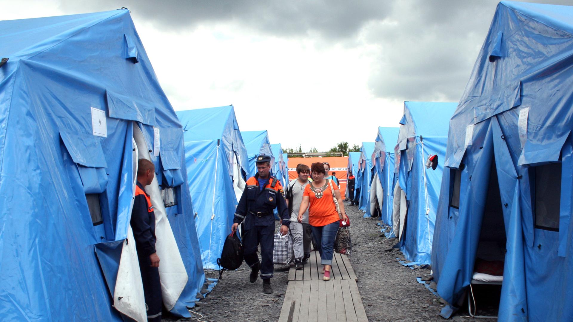 Neuankömmlinge aus dem Konfliktgebiet Ostukraine werden am 09.07.2014 von russischen Helfern im Flüchtlingslager in Nowoschachtinsk zu Zelten gebracht.