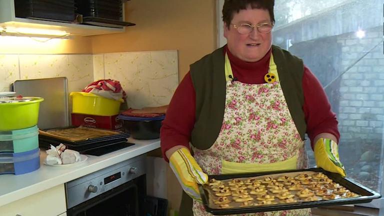 Die blinde Bäckerin Doris Hollnagel hält in ihrer Küche ein Blech voller Plätzchen in den Händen.
