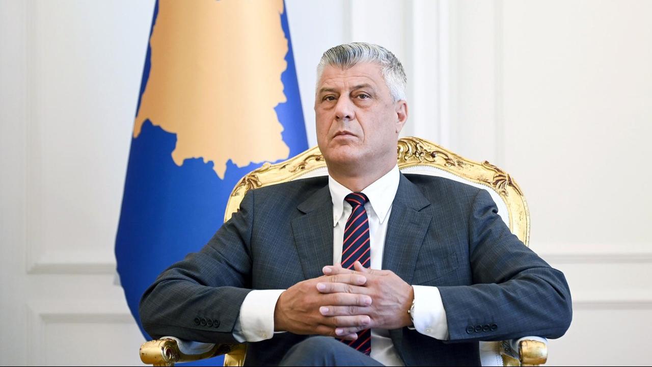 Kosovos ehemaliger Präsident Hashim Thaci im Jahr 2020. Er sitzt auf einem Stuhl, hinter ihm die kosovarische Fahne.