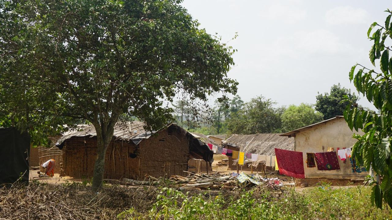 Zwischen Häusern in einem afrikanischen Dorf ist eine Wäscheleine gespannt, über der bunte Kleidung und Tücher hängen. 