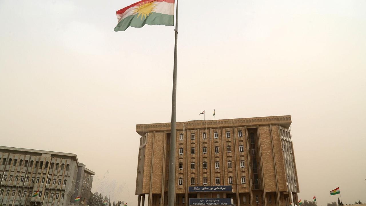 Außenansicht des beigefarbenen Gebäudes mit der Kurdenflagge davor.