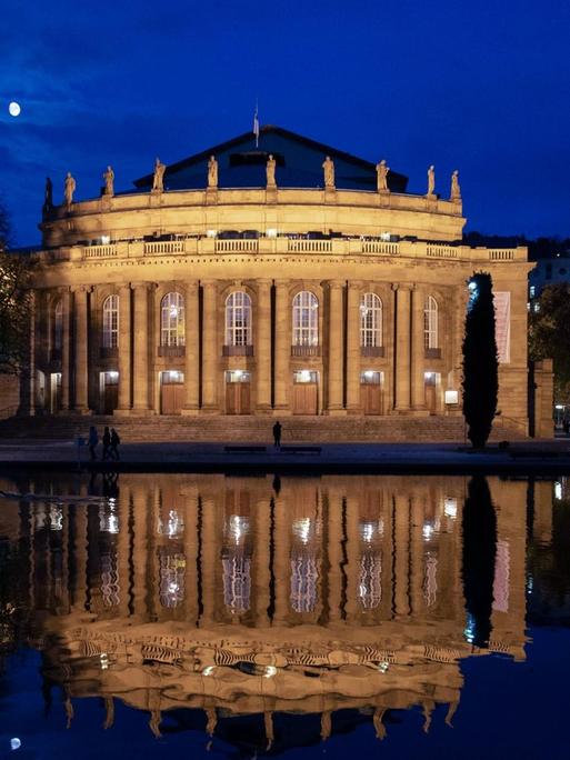 Die beleuchtete Staatsoper Stuttgart und der Mond spiegeln sich nachts im Eckensee.