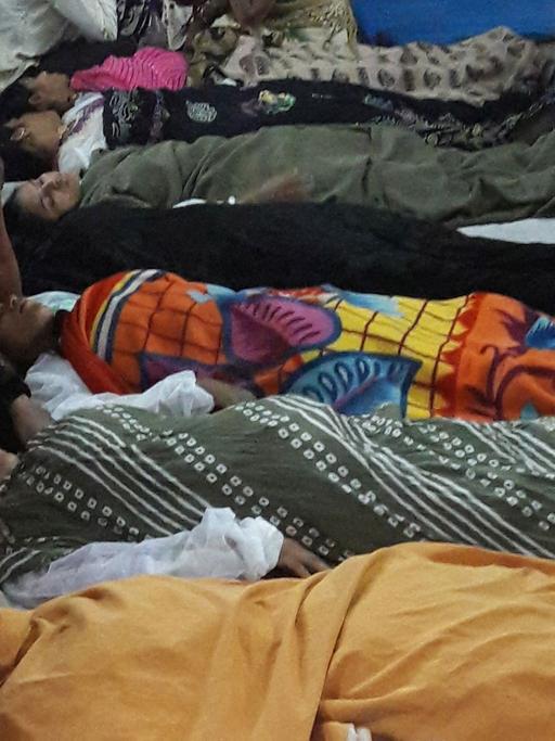 Frauen liegen nach der Operation schlafend auf dem Gang. An ihren Köpfen wachen Verwandte.